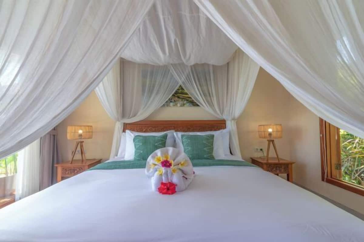A bed with a canopy, two bedside lamps, a green pillow, and a floral arrangement on the bed.