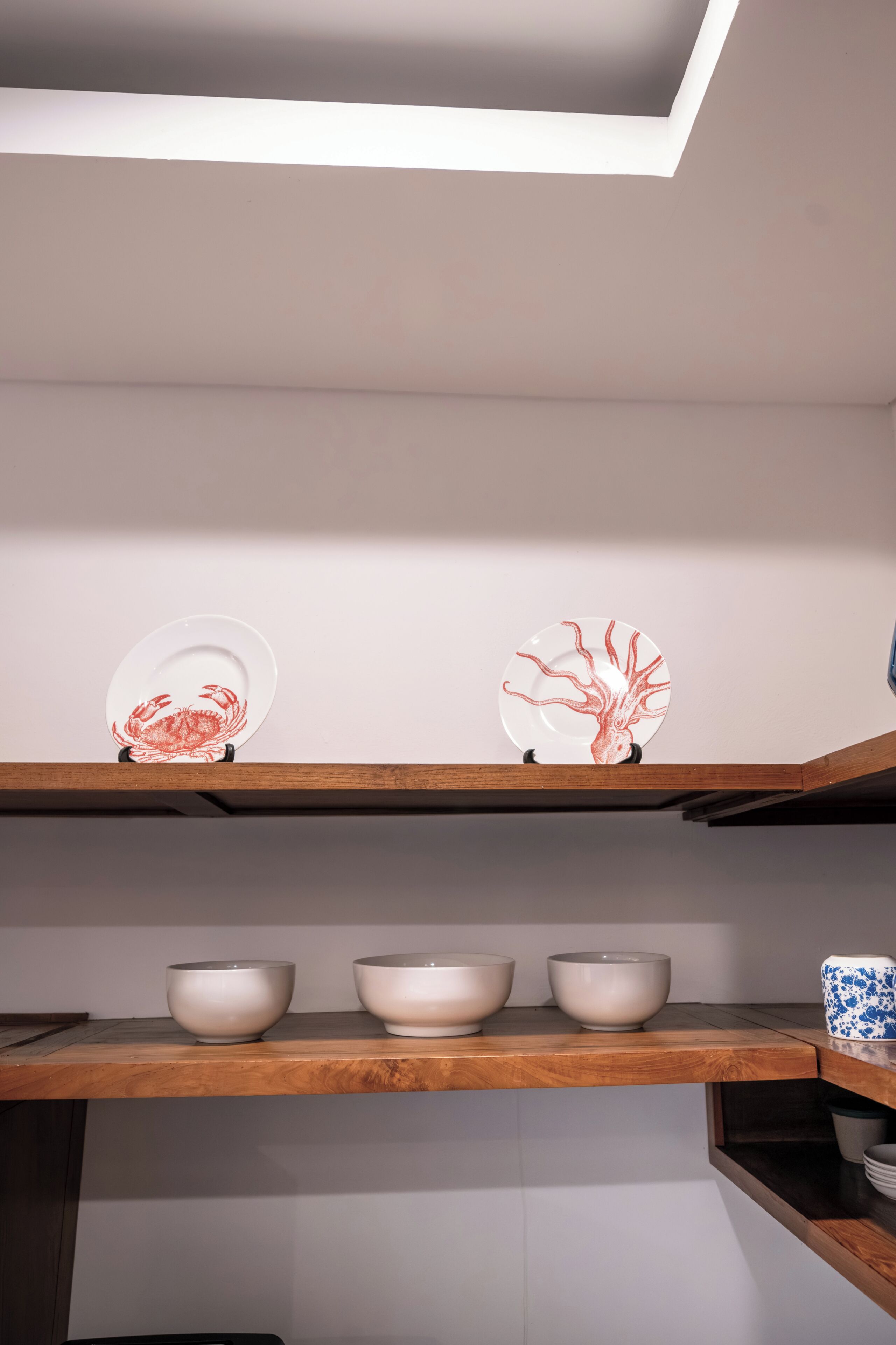 Une étagère de cuisine avec trois bols blancs et deux assiettes décoratives ornées de motifs rouges.