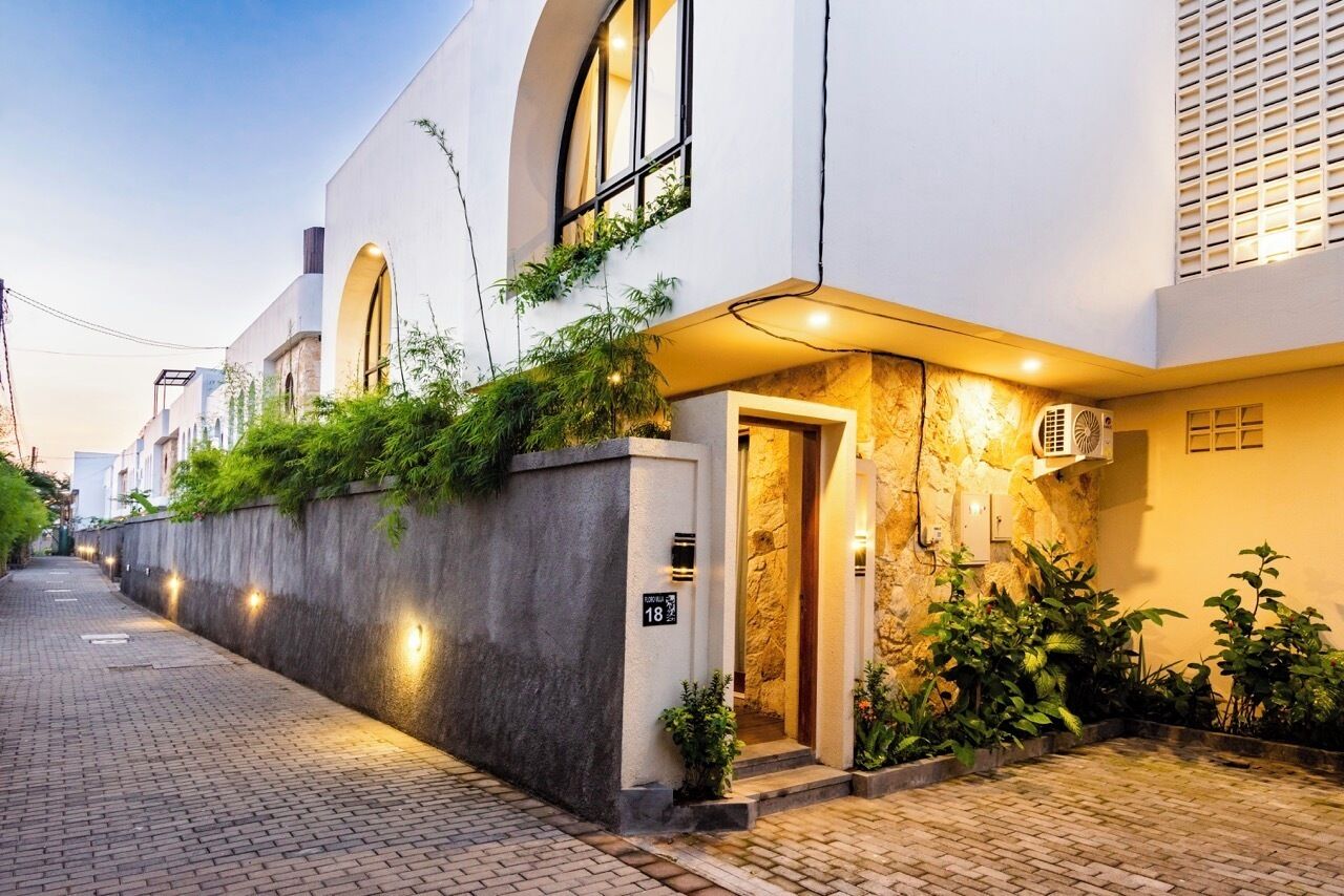 Un edificio moderno con un sendero pavimentado, un muro de piedra con vegetación y una entrada bien iluminada.