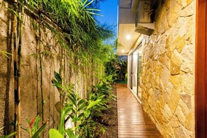 Un étroit sentier bordé d’un mur de bambou et d’un mur de pierre, menant à l’entrée d’un bâtiment.