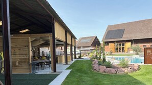 A covered outdoor area with a pool, a patio with tables and chairs, and a well-maintained lawn.