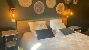 A neatly made bed with white linens and multiple pillows, flanked by two bedside tables with woven placemats.