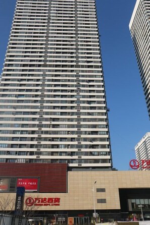 Um edifício alto com vários andares, área comercial na base com placas de sinalização e um céu azul claro ao fundo.