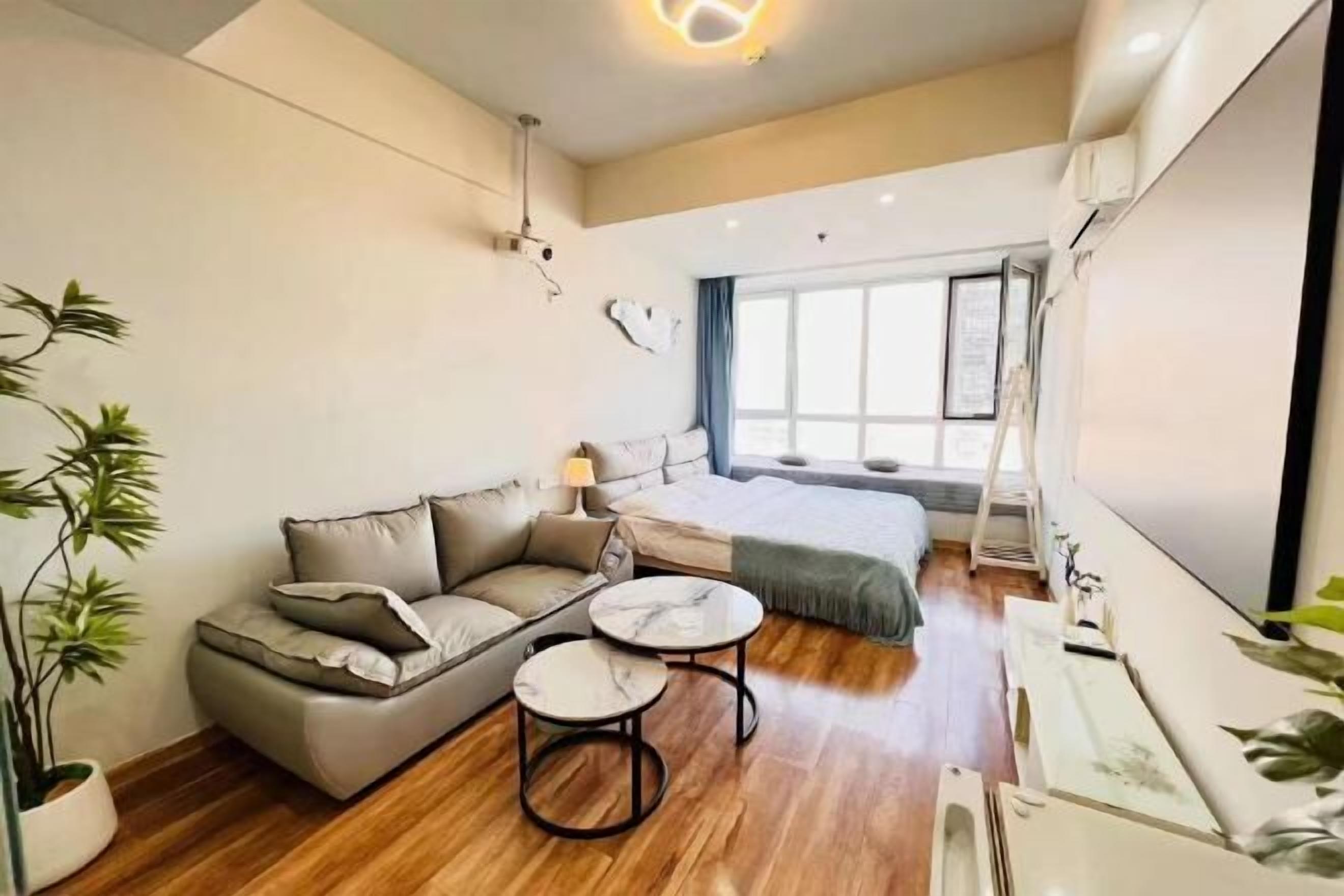 A modern hotel room with a sofa, two round tables, a bed, and large windows.