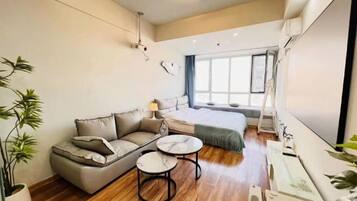 A modern hotel room with a sofa, two round tables, a bed, and large windows.
