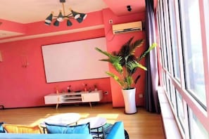 A room with a large window, a whiteboard, a plant, and a white entertainment unit.