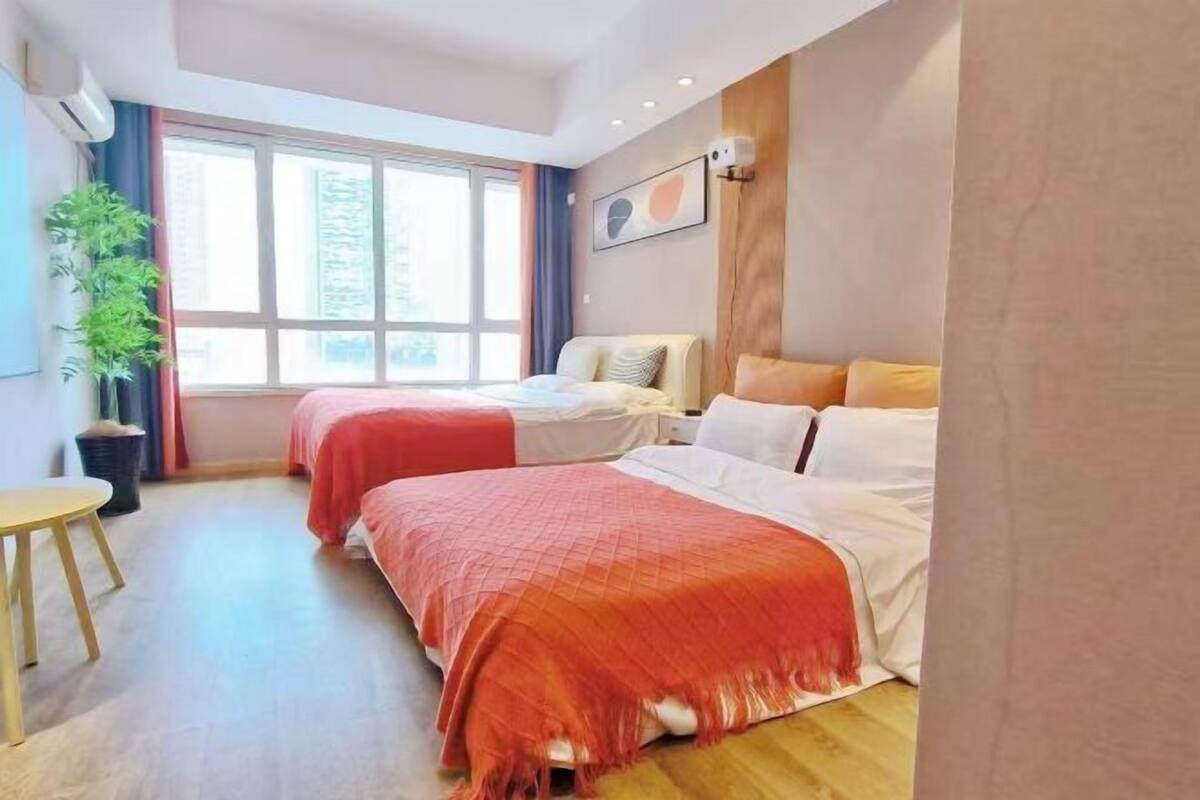A hotel room with two beds, a large window, a plant, and a small table.