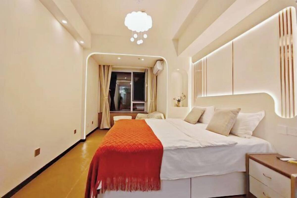 A hotel room with a bed, bedside table, and a window with curtains.