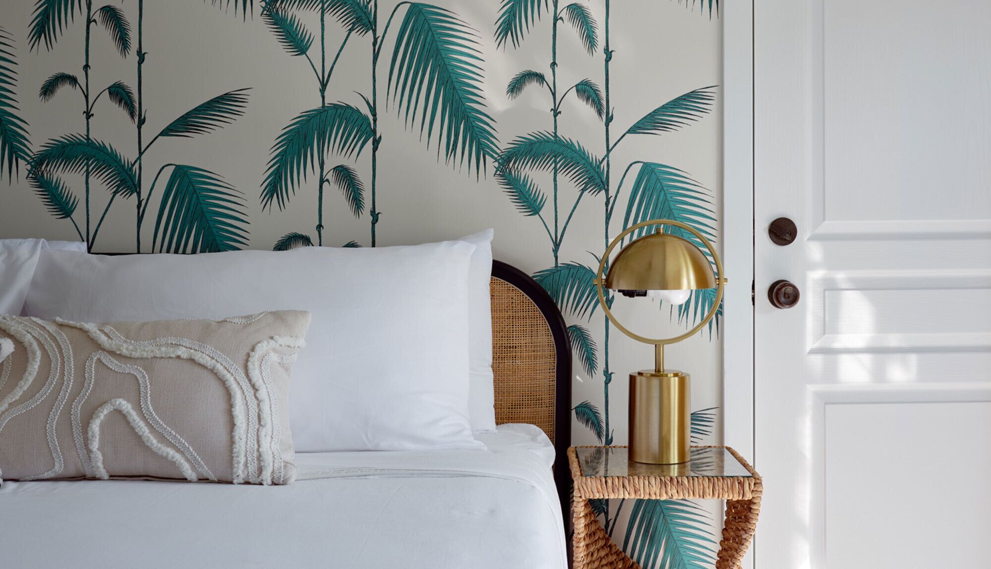 A bedroom with a bed, pillows, a nightstand with a lamp, and a door.