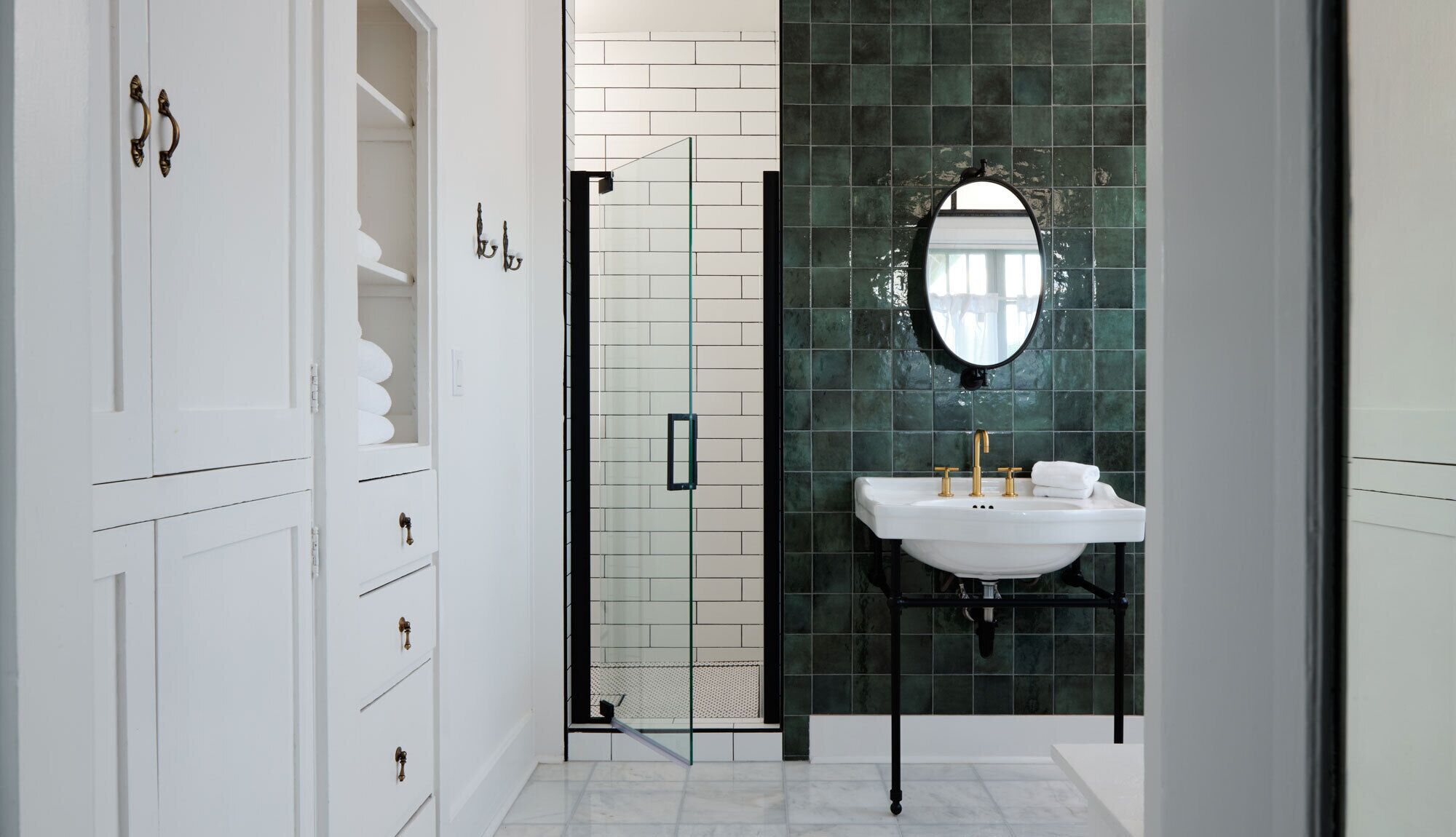 A bathroom with a white vanity, a glass shower enclosure, and a green tiled wall.