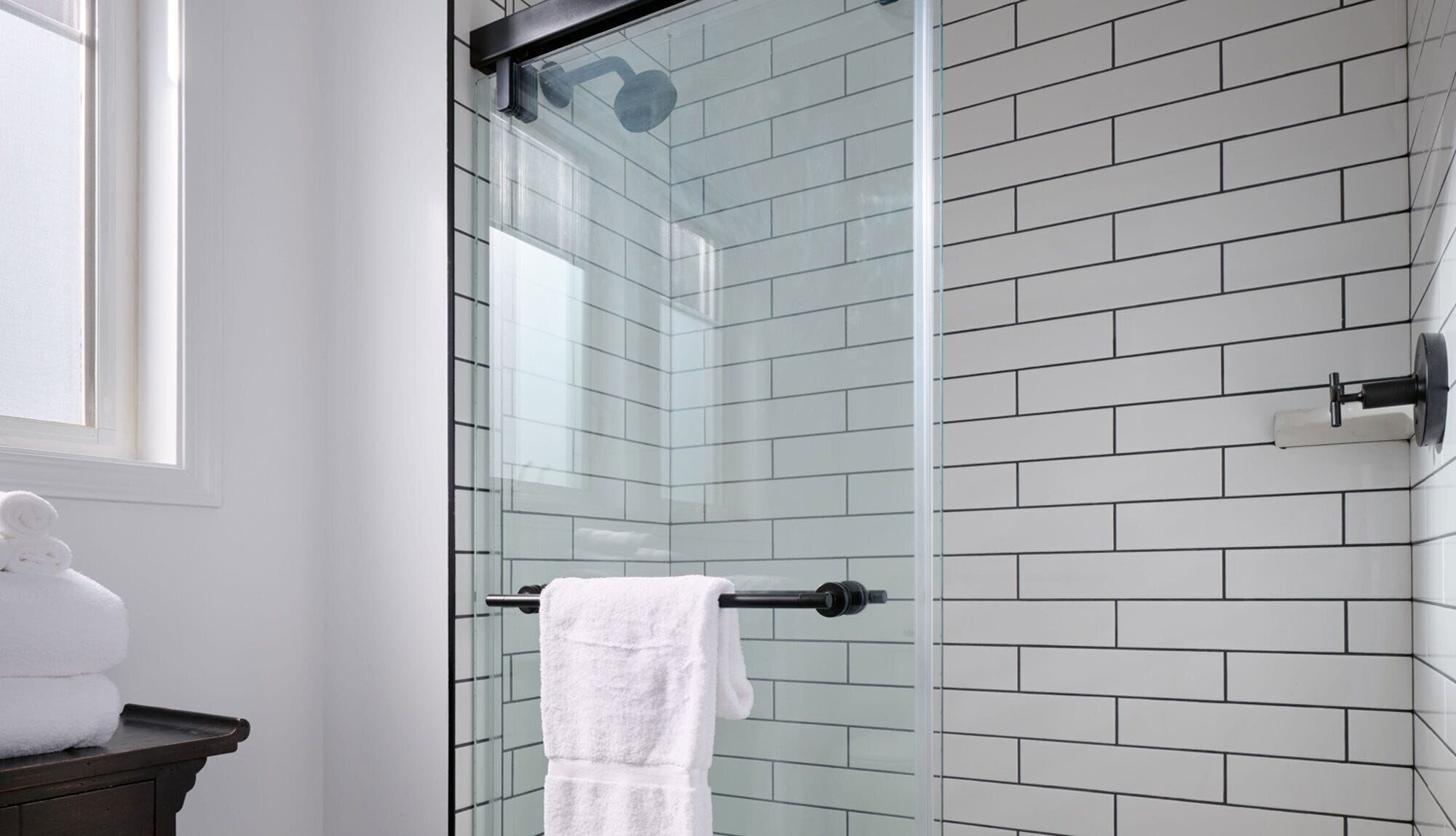 Un baño moderno con cabina de ducha de vidrio, paredes con azulejos blancos y un toallero a la vista.