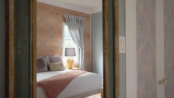 A bedroom with a bed, a window with curtains, a lamp, and a mirror.