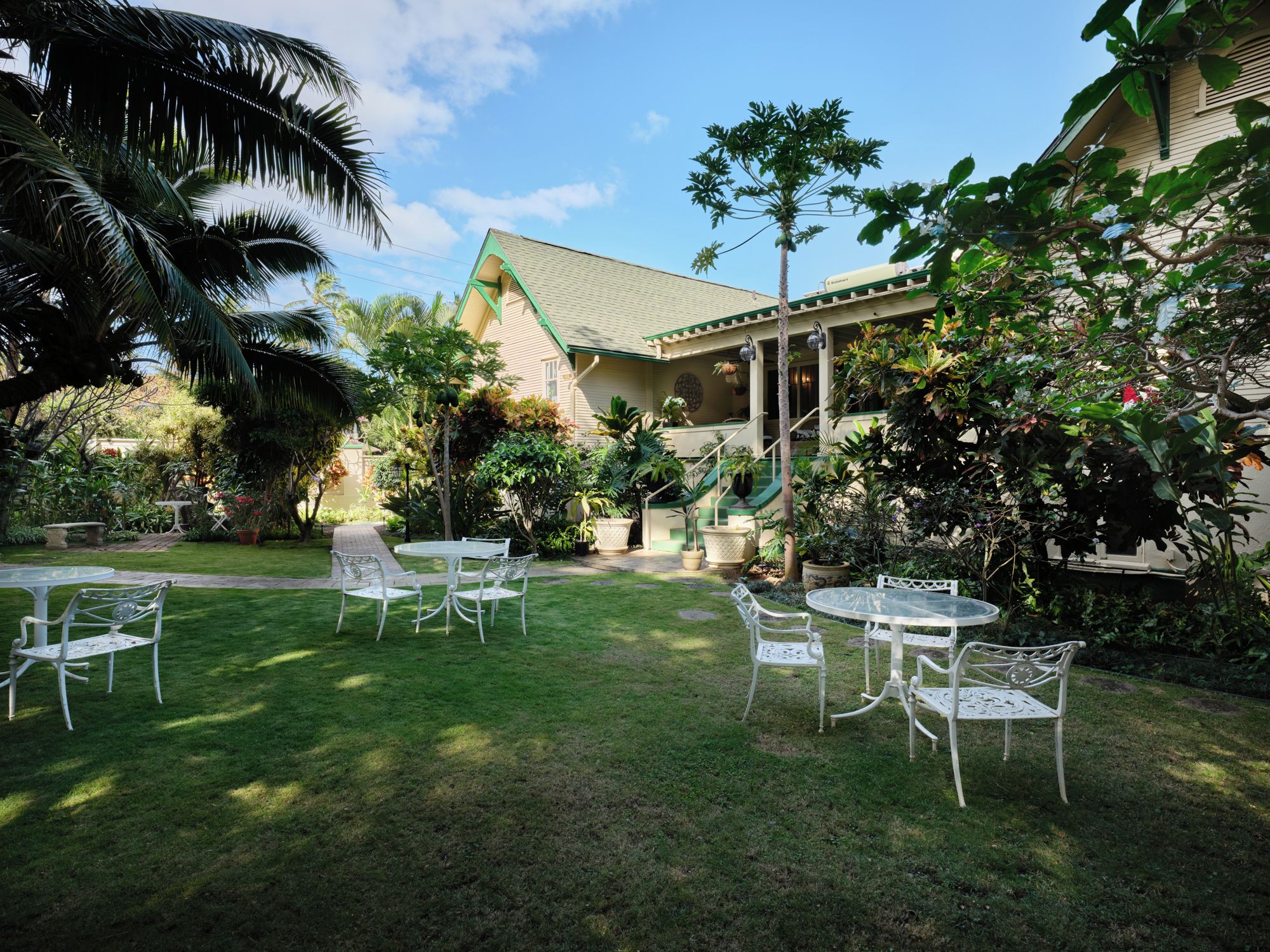 A well-maintained outdoor area with a patio, chairs, and tables, surrounded by lush greenery and a building with a green roof.