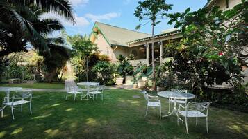 A well-maintained outdoor area with a patio, chairs, and tables, surrounded by lush greenery and a building with a green roof.