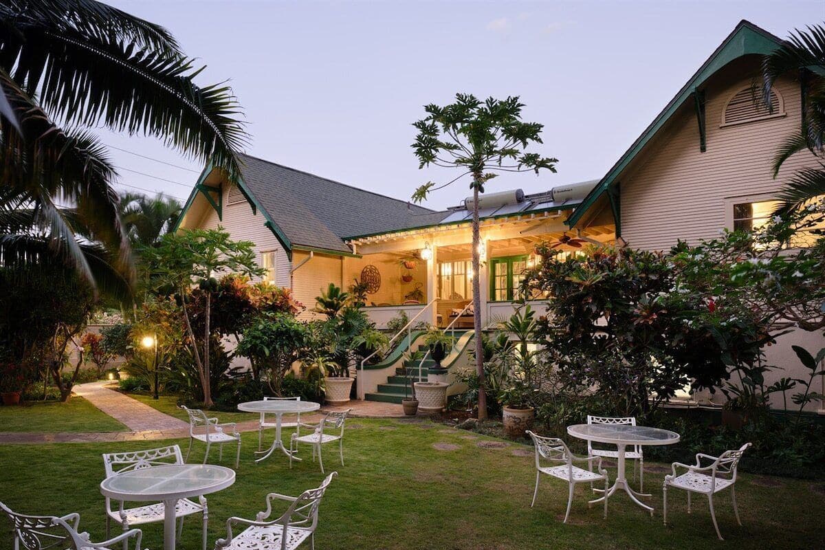 A well-maintained outdoor patio area with multiple tables and chairs, surrounded by lush greenery and a staircase leading to a building.
