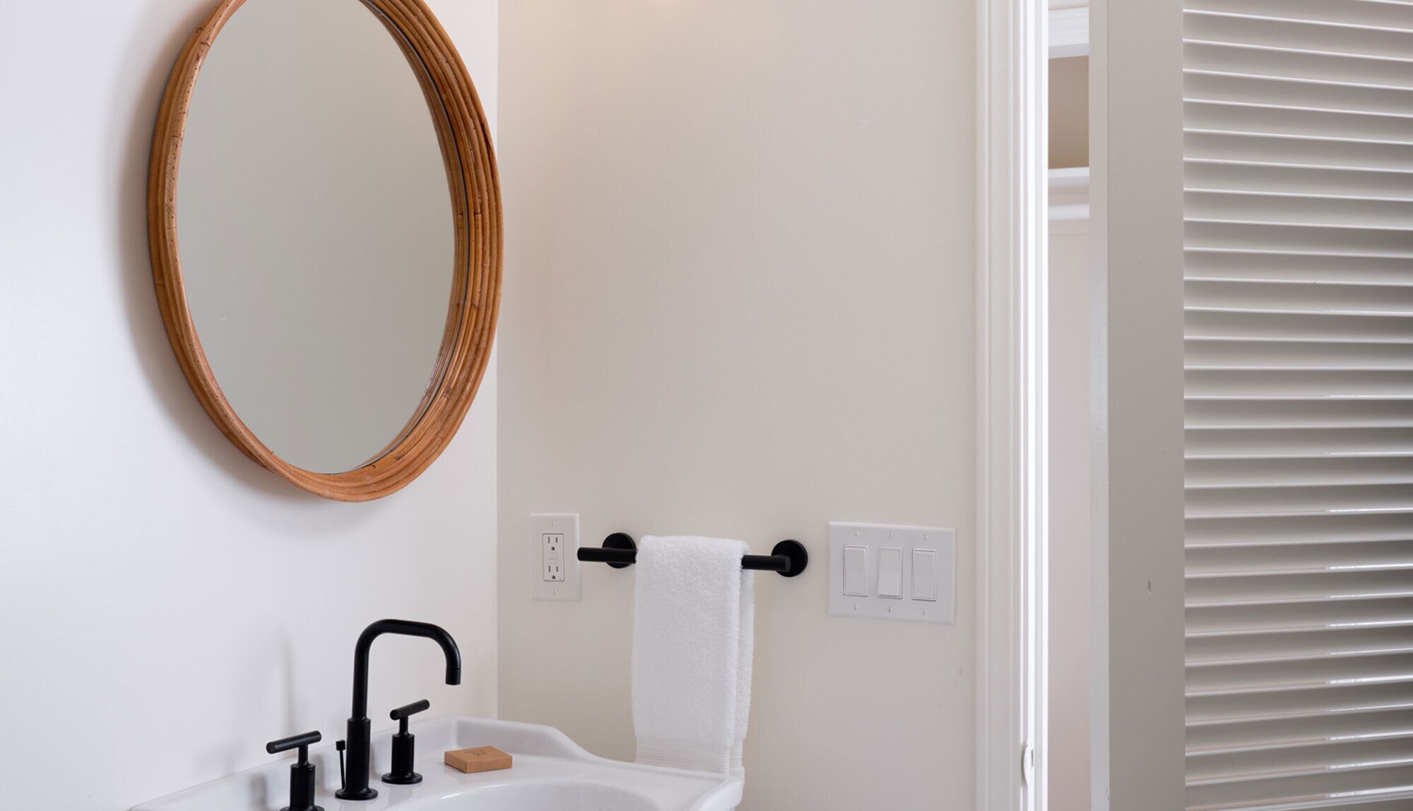 Un baño con un lavamanos blanco, grifo negro y un espejo con marco de madera.