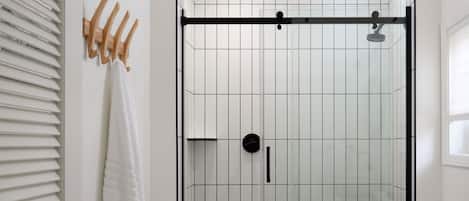 A bathroom with a white tiled shower enclosure, a towel rack with a white towel, and a toilet with a toilet paper holder.