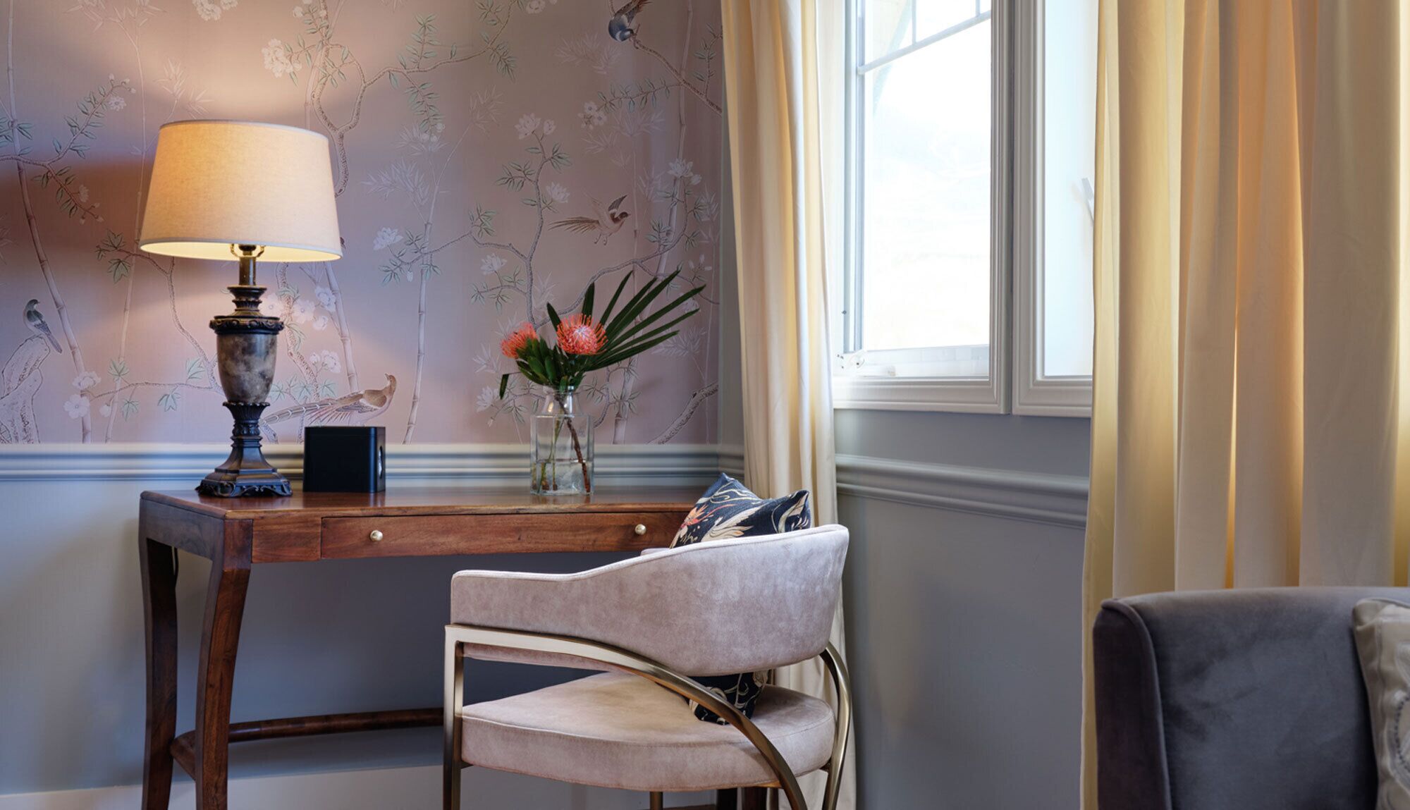 A room with a wooden desk, a lamp, a vase with flowers, and a chair.