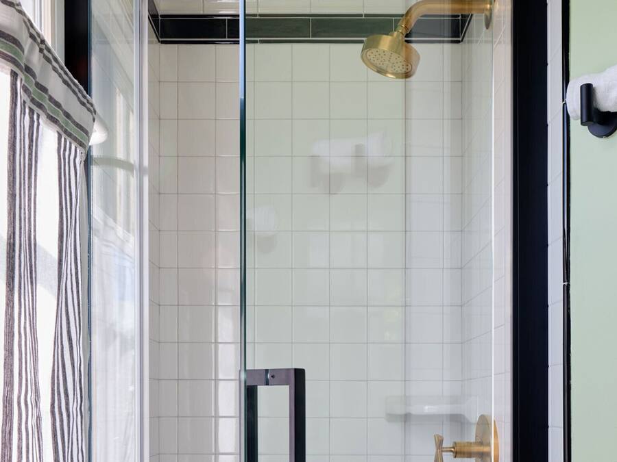 Ein modernes Badezimmer mit Duschkabine aus Glas, weißen Fliesen und einem Handtuchhalter an der Wand.