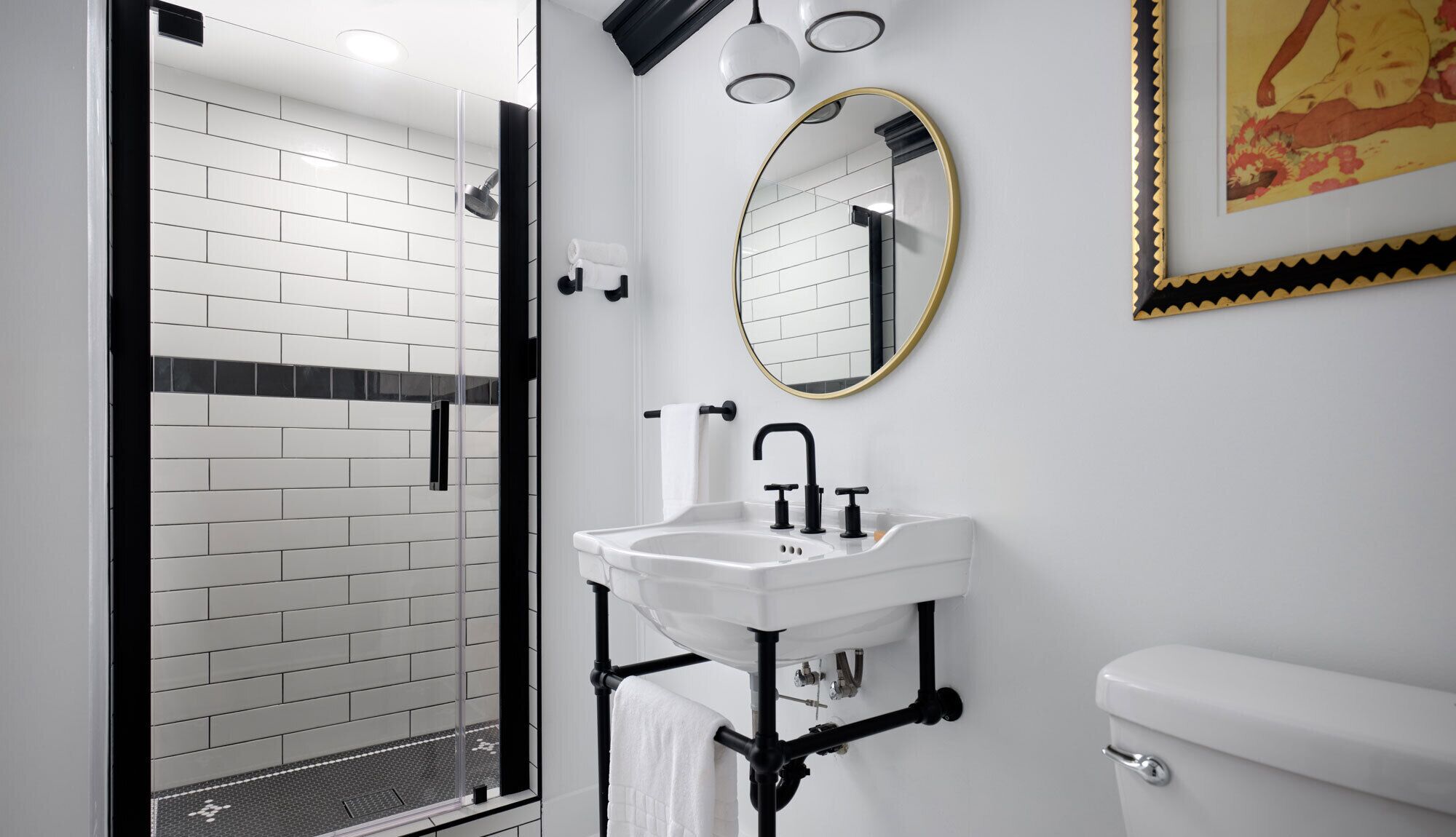 Un baño moderno con ducha de azulejos blancos, lavabo blanco con accesorios negros y un inodoro.