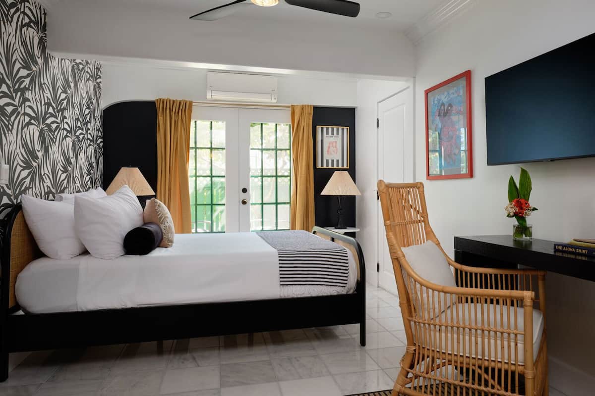 A bedroom with a bed, a chair, a desk, a TV, and artwork on the walls.