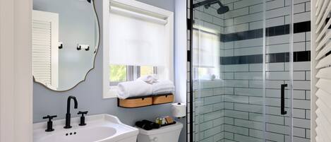 A modern bathroom with a white sink, a mirror, a toilet, and a glass shower enclosure.