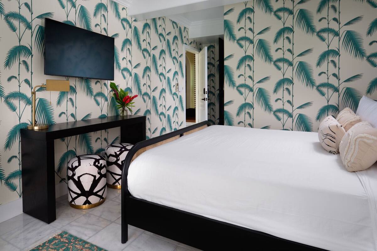 A bedroom with a bed, a TV mounted on the wall, a console table, and a decorative vase.