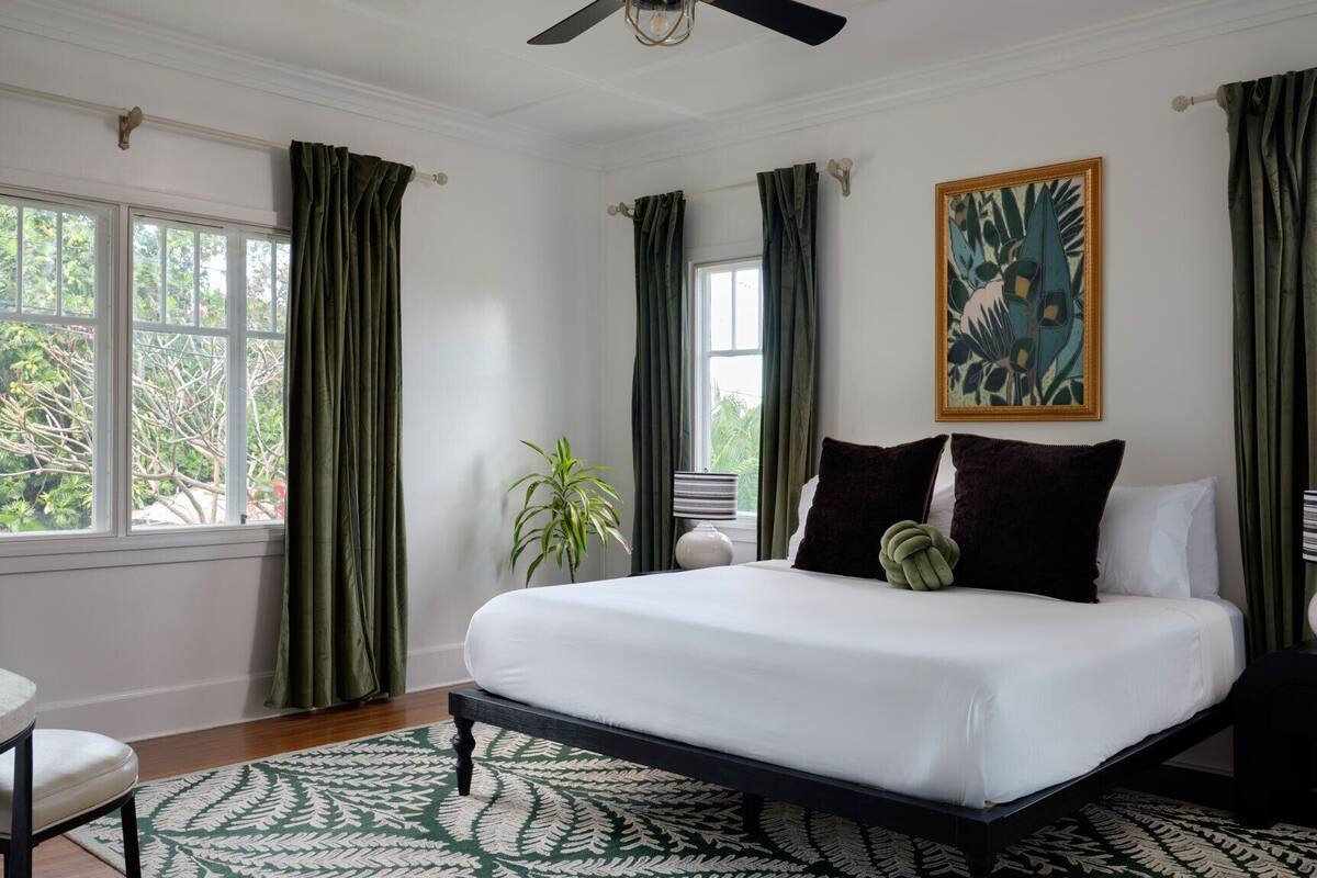 A spacious bedroom with a large bed, green curtains, a ceiling fan, and a fern-patterned rug.