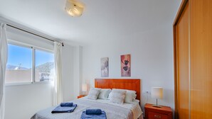 A bedroom with a large bed, two wall-mounted lamps, a wooden wardrobe, and a window with curtains. - Mascarat by Interhome (Calpe/Calp)