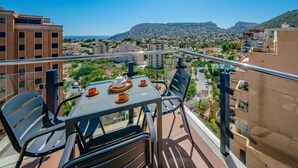 A balcony with a table set for two, overlooking a cityscape with buildings and a mountain in the distance. - Mascarat by Interhome (Calpe/Calp)