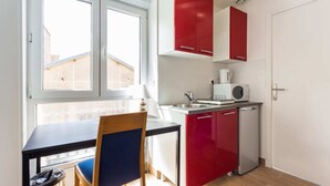 A compact kitchen with a dining table, a chair, a small refrigerator, and red cabinets. - Résidence MALAKOFF (Malakoff)