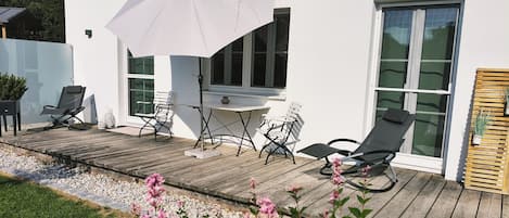 Une terrasse avec des meubles d’extérieur, une table et un parasol blanc.