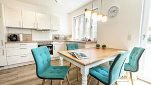A modern kitchen with white cabinets, a wooden table, teal chairs, and a clock on the wall.