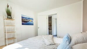 A bedroom with a bed, a ladder, a plant, and a painting on the wall.