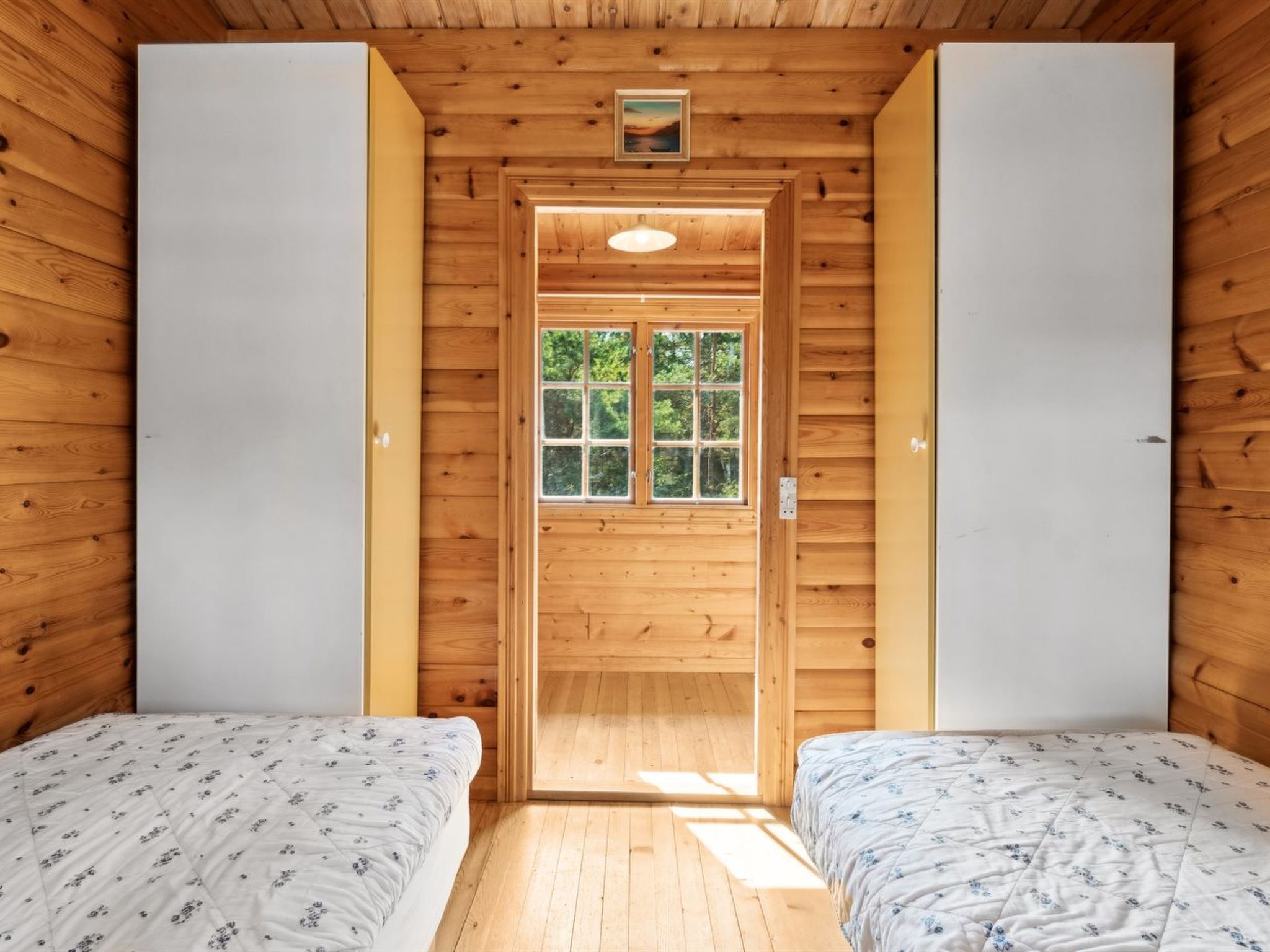 Eine Holzhütte mit zwei Betten, Holzwänden, einem Fenster mit Blick ins Grüne und einem kleinen Bild an der Wand.