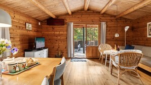 Ein gemütliches Blockhaus-Interieur mit einem Holzespeisetisch, Stühlen, einem Fernseher und einer Couch.