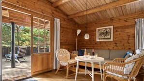 Ein Holzblock-Innenraum mit Essbereich, Korbmöbeln, Deckenventilator und einem großen Fenster mit Vorhängen.