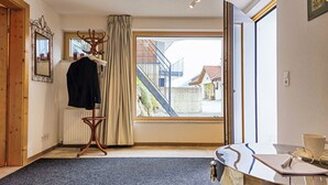 A room with a large window, a coat rack with clothes, a radiator, and a table with a cup and glasses. - Sonnenseite by Interhome (Kappl)