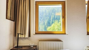 A bedroom with a window overlooking a forest, a bedside table with a lamp, and a radiator. - Sonnenseite by Interhome (Kappl)