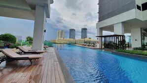 A rooftop pool with lounge chairs, a view of modern buildings, and a cloudy sky. - MidValley MegaMall View Southkey Mosaic 2BR 2FREE By Natol (Johor Bahru)