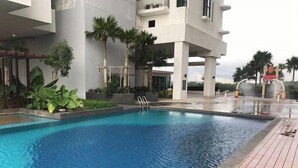 A swimming pool with a wooden deck, surrounded by palm trees and a modern building. - MidValley MegaMall View Southkey Mosaic 2BR 2FREE By Natol (Johor Bahru)