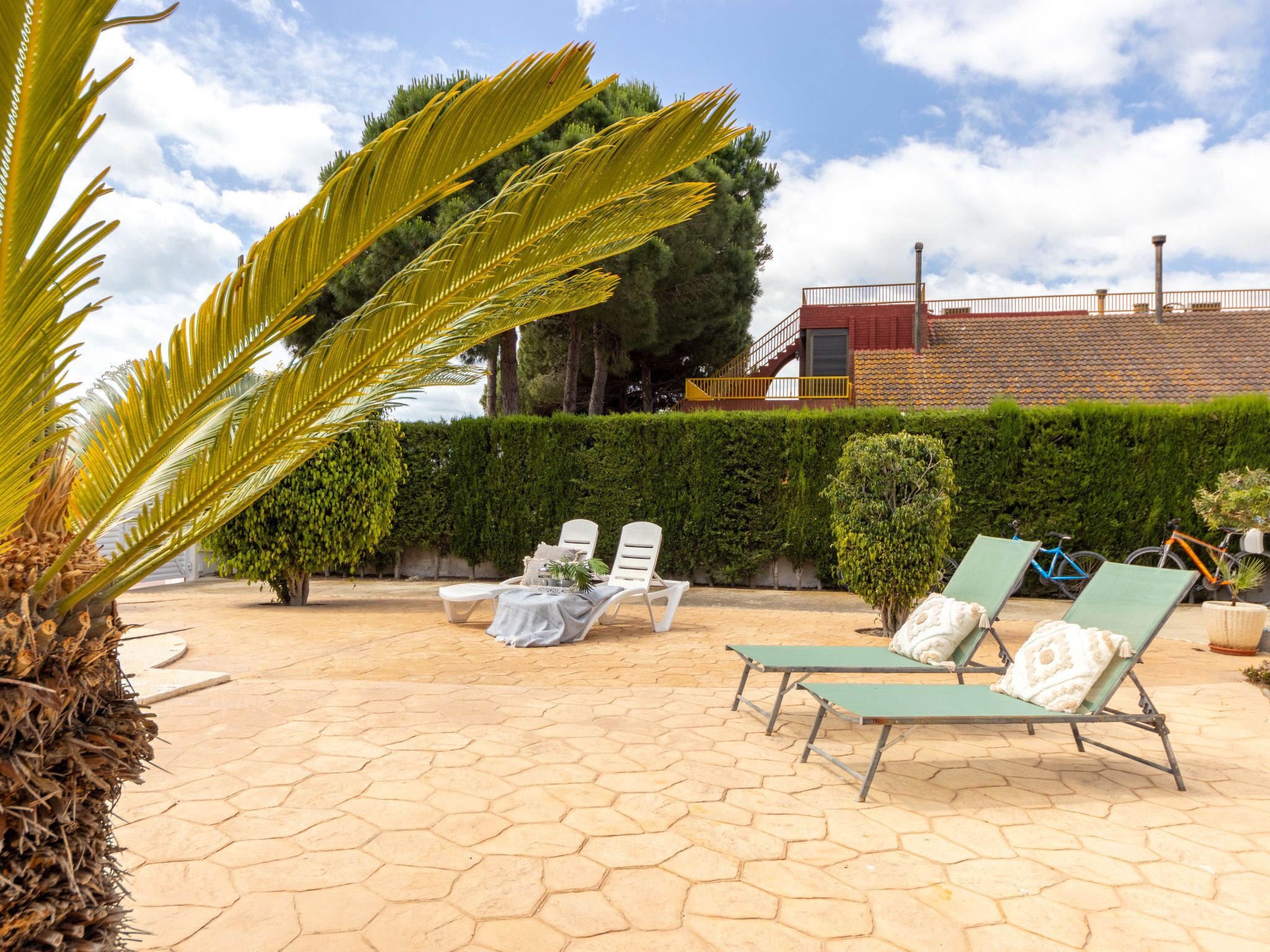 Un patio al aire libre con baldosas hexagonales, sillones de descanso y un seto bien cuidado.
