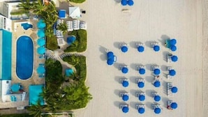 Vue aérienne d’un hôtel situé en bord de mer, doté de plusieurs piscines, de transats et de palmiers.