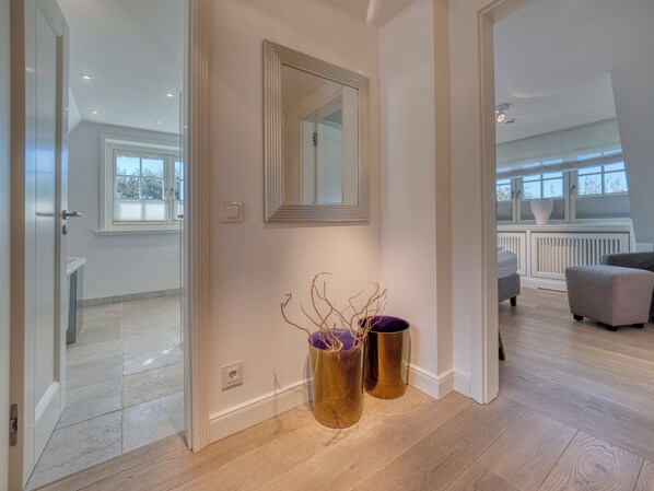 Ein moderner Flur mit Glastür zu einem Badezimmer, einem Spiegel an der Wand und zwei dekorativen Vasen.