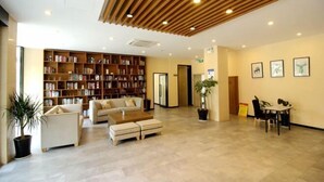 A spacious lobby with a large bookshelf, a seating area with a sofa and ottomans, a coffee table, and a dining table with chairs.