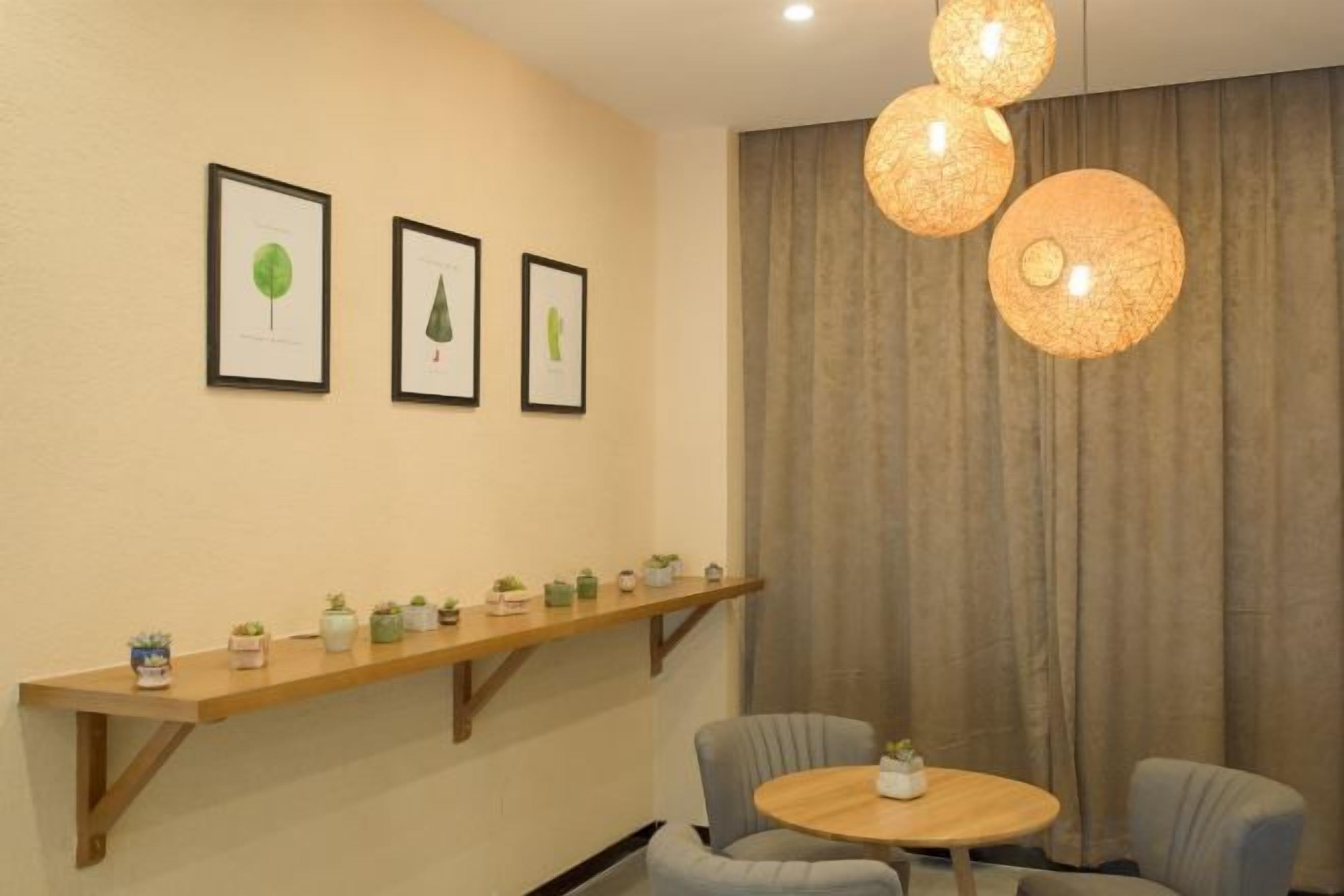A room with a round wooden table, two chairs, a shelf with potted plants, and three framed pictures on the wall.