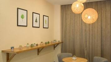 A room with a round wooden table, two chairs, a shelf with potted plants, and three framed pictures on the wall.