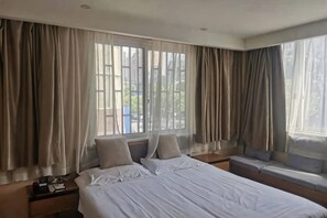 Et hotelværelse med seng, sengeborde og et vindue med gardiner.
