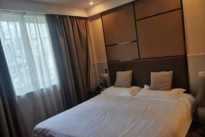 A hotel room with a large bed, a nightstand, and a window with curtains.