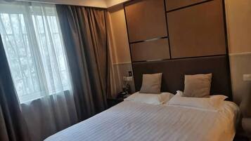 A hotel room with a large bed, a nightstand, and a window with curtains.